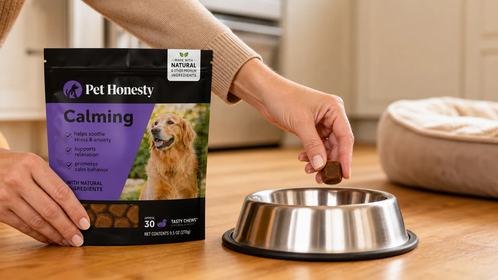 A hand placing a calming chew treat into a dog's food bowl next to a cozy dog bed